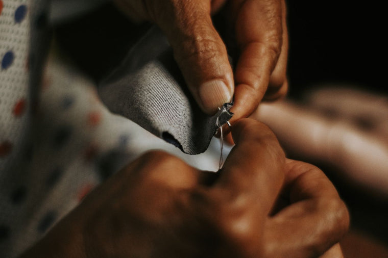 Close-up of hands mending grey fabric with a needle and thread