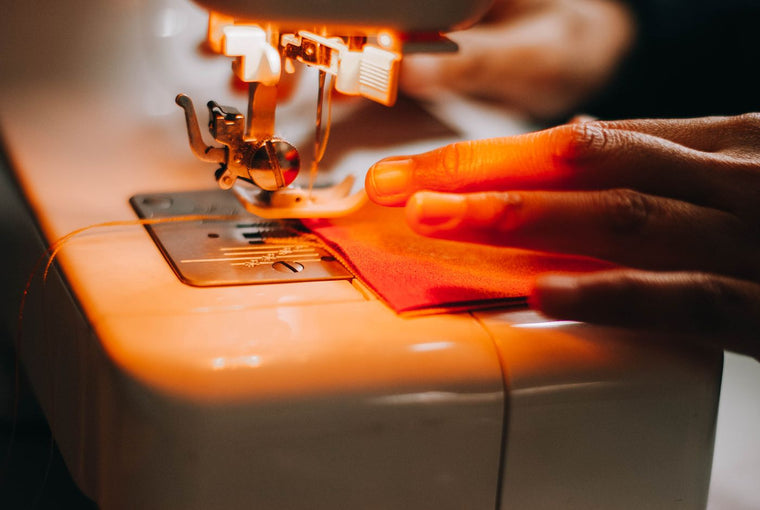 Close-up of a sewing machine stitching red fabric with the upper thread feeding to the needle