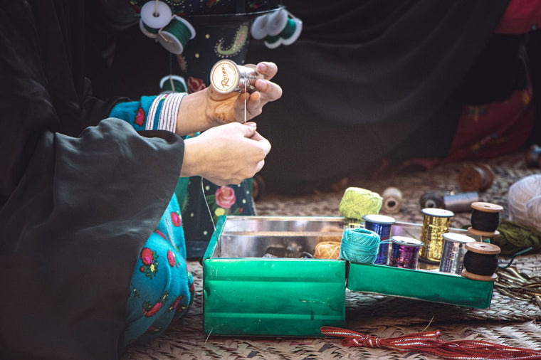 Hands handling thread beside an open green sewing-supply box with spools and yarn