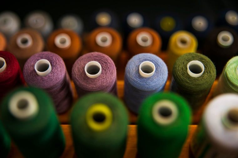 Rows of assorted coloured sewing thread spools for choosing a shade to match fabric