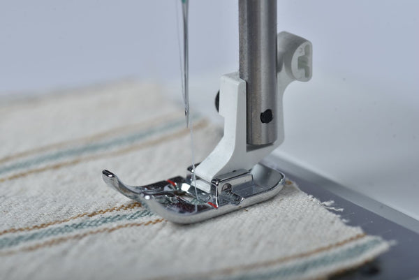 Sewing machine needle stitching fabric with thread