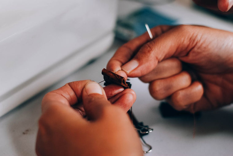 Hands guiding a threaded sewing needle through fabric during a hand-sewing repair