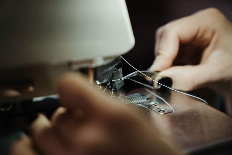 Hands threading the upper thread on a sewing machine near the needle and tension area