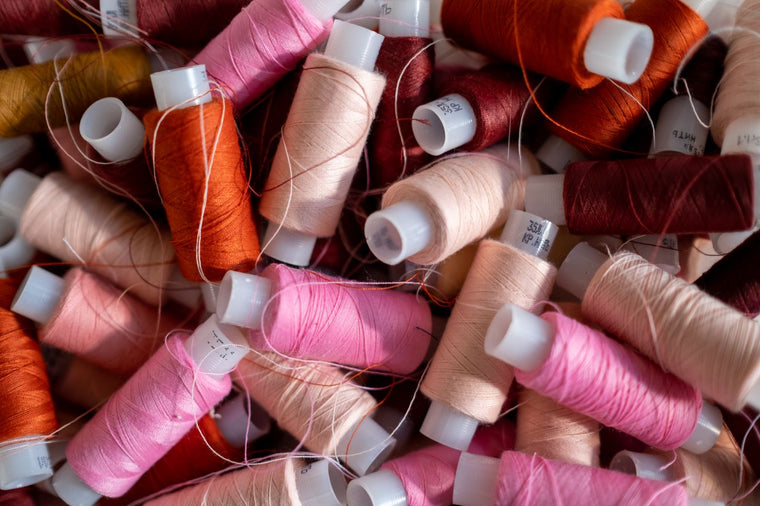 A pile of colourful sewing thread spools in soft pink, cream and warm tones